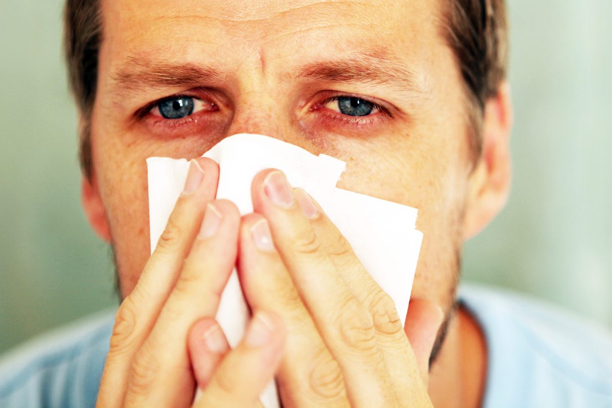 man blowing nose with allergies
