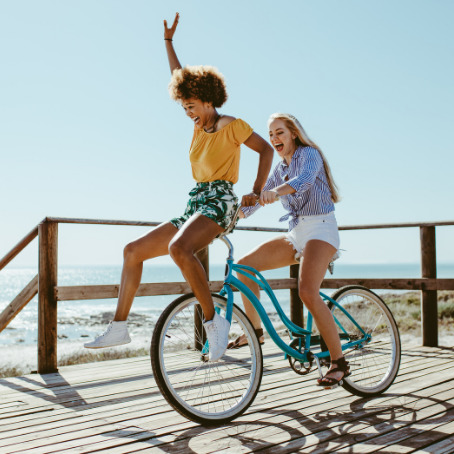 Two girl friends have fun riding a bike on a pier